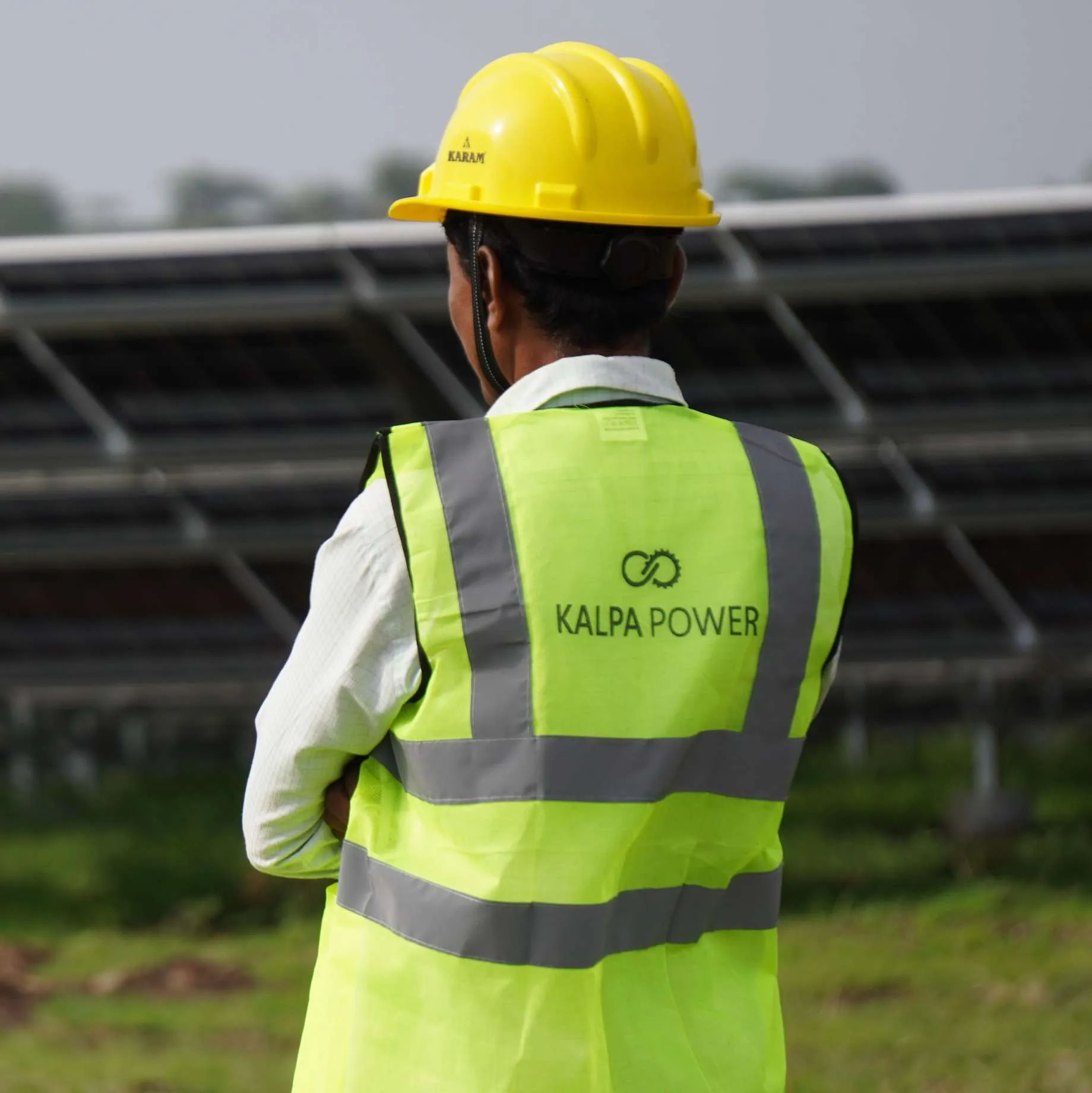 A Kalpa Power engineer in a hard hat surveying rows of solar panels